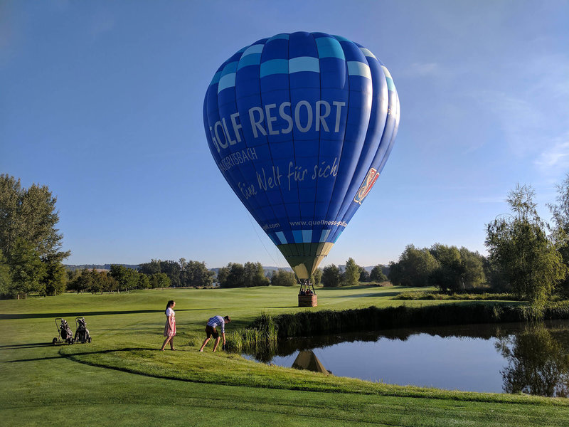 Großer Ballon auf einem Golfplatz hinter einem Teich und Golfern