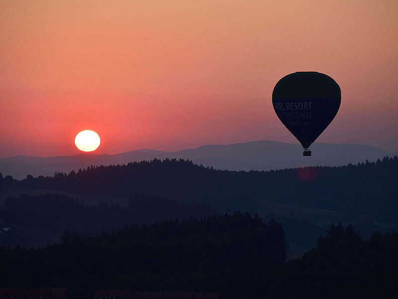 Sonnenuntergang hinter kleinen Bergen und Wäldern mit Ballon im Vordergrund