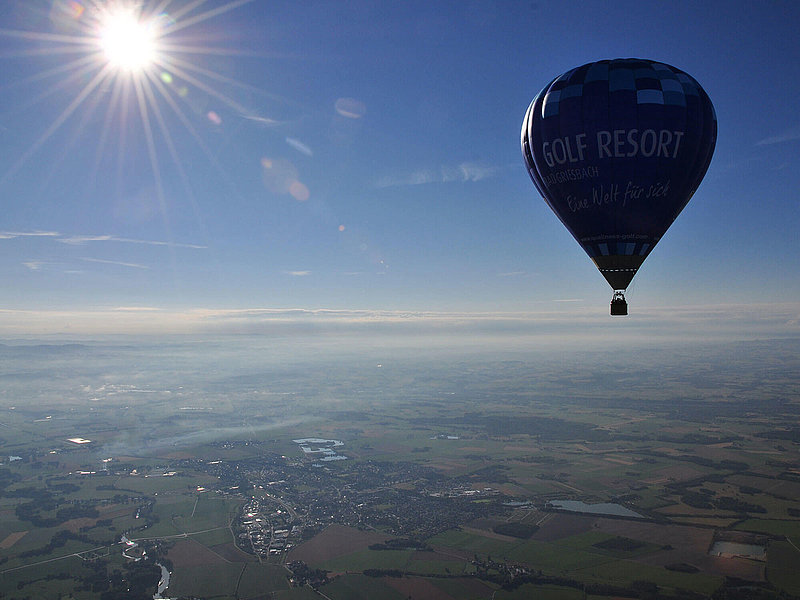 Heißluftballon fährt über flache Landschaften bei blauem Himmel und Sonnenschein
