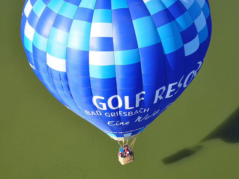 Blauer Ballon mit Karo-Muster oben über einem grünen Feld