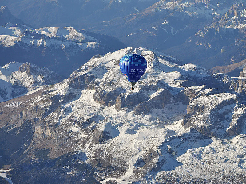 Steinige und verschneite Berge hinter einem blauen Heißluftballon