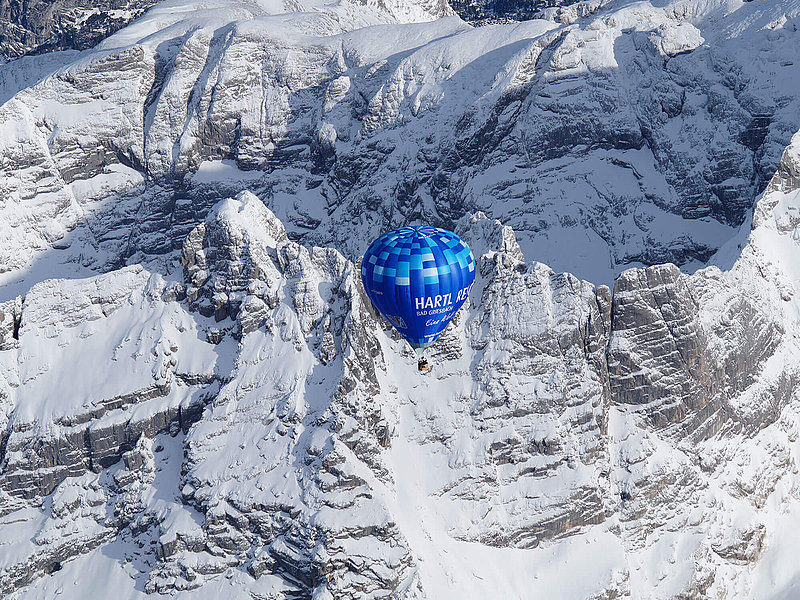 Heißluftballon vor einer steilen zugeschneiten Bergwand