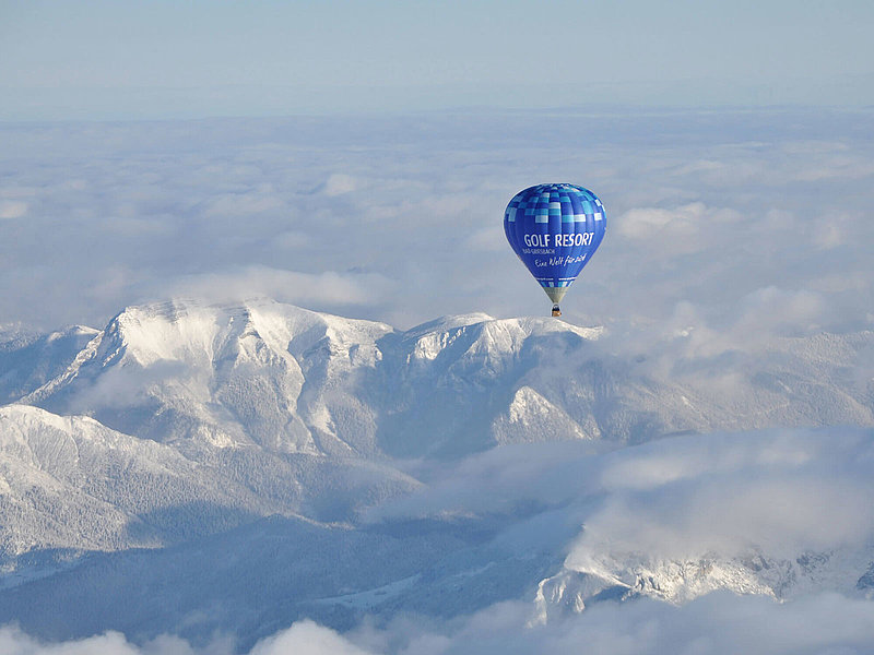 Blauer Heißluftballon über leicht bewölkten Berggipfeln in den Alpen