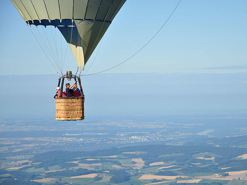 Pilot steuert den Ballon, die Passagiere genießen die Aussicht auf Felder und Städte