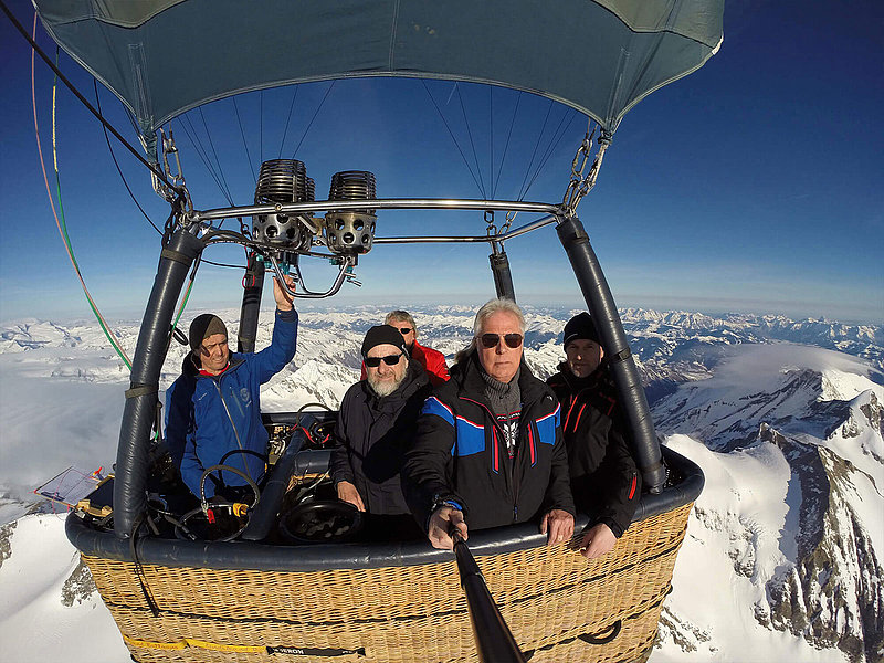 Passagiere und Pilot fotografieren sich selbst im Korb über den Alpen