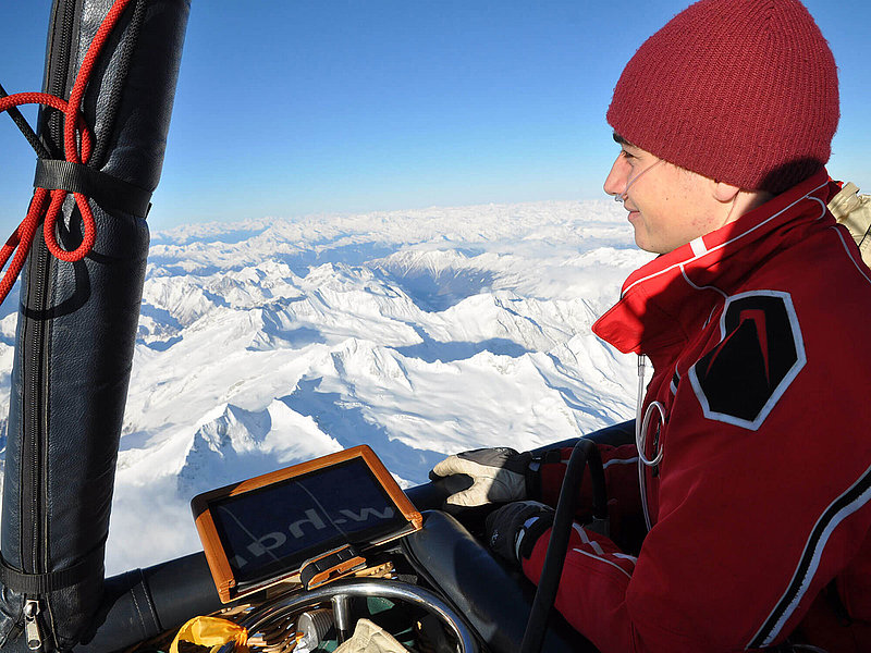 Pilot Lukas mit Sauerstoffschlauch in der Nase über schneebedeckten Bergen