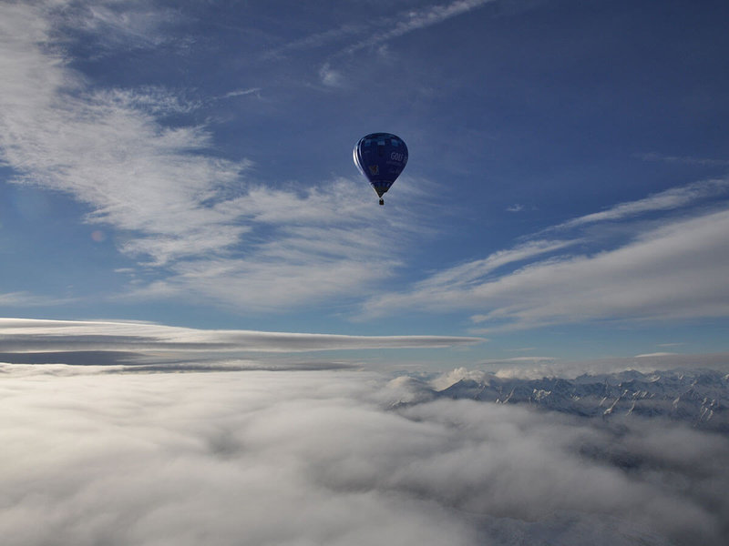 Blauer Heißluftballon über den Wolken und Berggipfeln